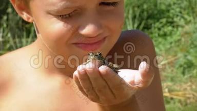 小男孩手里拿着一只青蛙，在河边的海滩上用手指敲击蟾蜍
